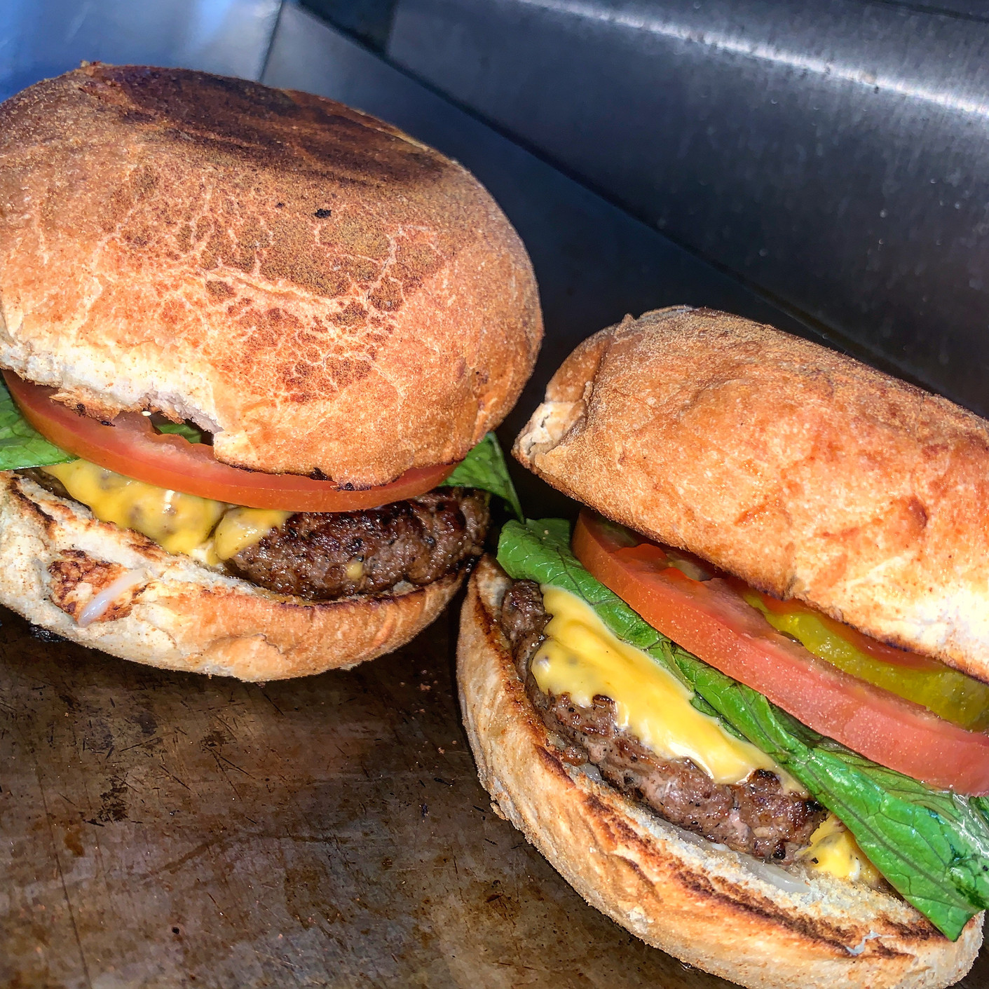 Two burgers with beef patties, cheese, lettuce, tomato, and pickles on toasted buns