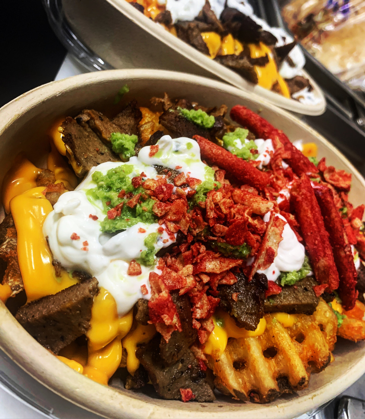 Overhead shot of a loaded bowl of waffle fries topped with chopped meat, shredded cheese sauce, sour cream, and green sauce