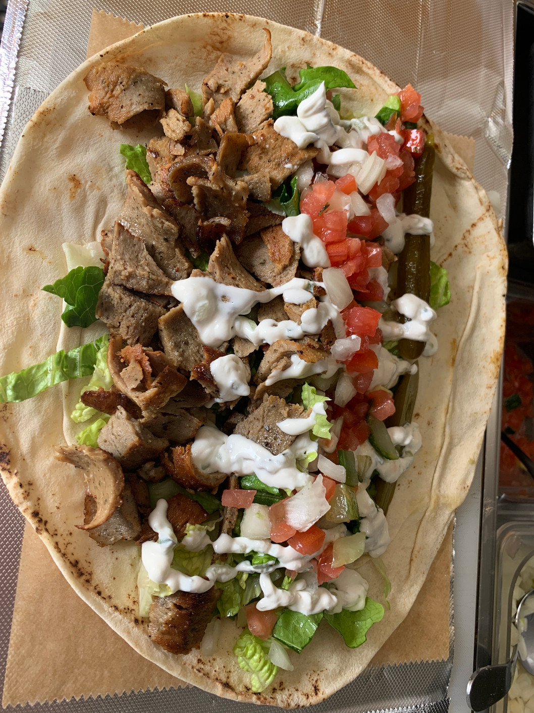 Overhead view of a flatbread filled with sliced grilled meat, shredded lettuce, diced tomato, onion, pickles, and a creamy sauce